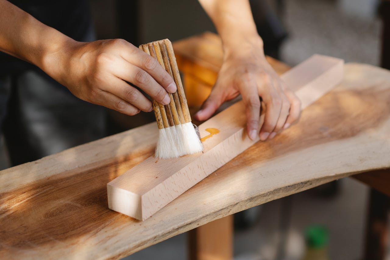 A craftsman applies oil to a wooden plank using a brush, showcasing skilled carpentry techniques.